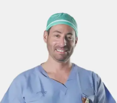 Portrait of Dr. Amir Kershenovich in surgical scrubs and cap, smiling on a white background